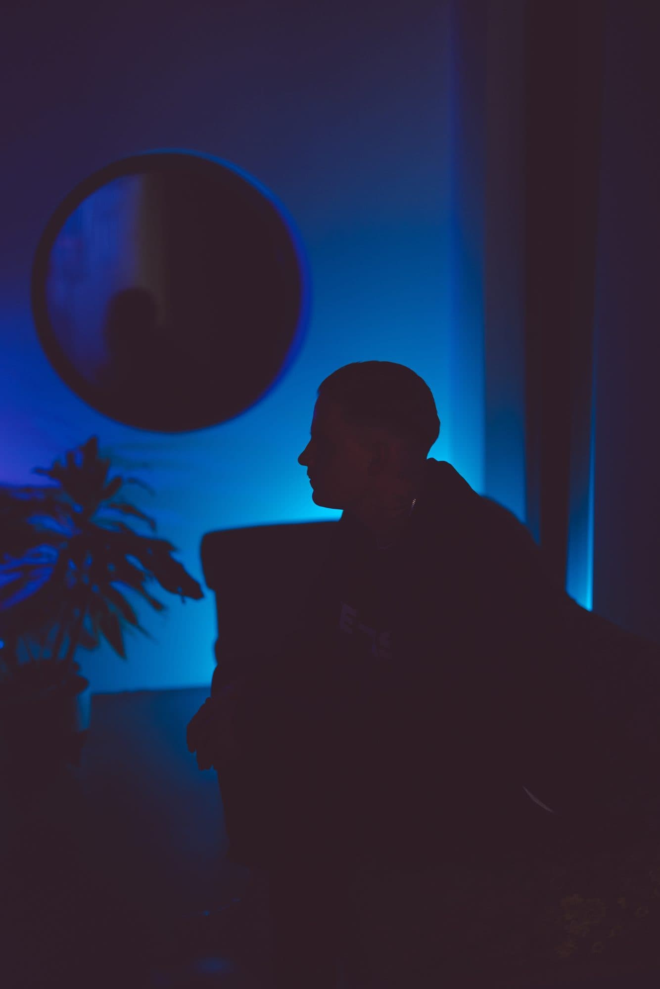 Silhouette einer Person im Profil vor blau beleuchteter Wand mit rundem Spiegel und Zimmerpflanze im ROMI Studio