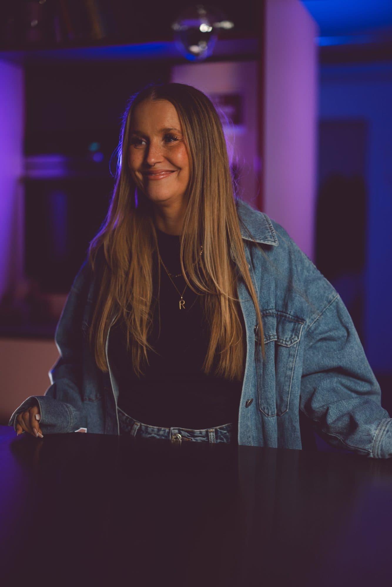 Lena, Mitinhaberin von ROMI, lachend hinter der Theke im blau-pink beleuchteten Studio